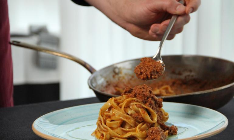 Pasta with ragù served on a plate, spoon adding more sauce.