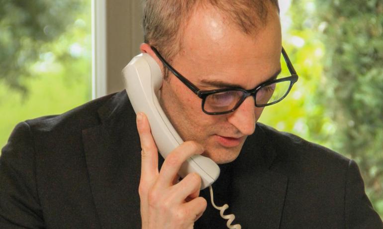 Man in suit and tie on the phone, wearing glasses and an ID badge.