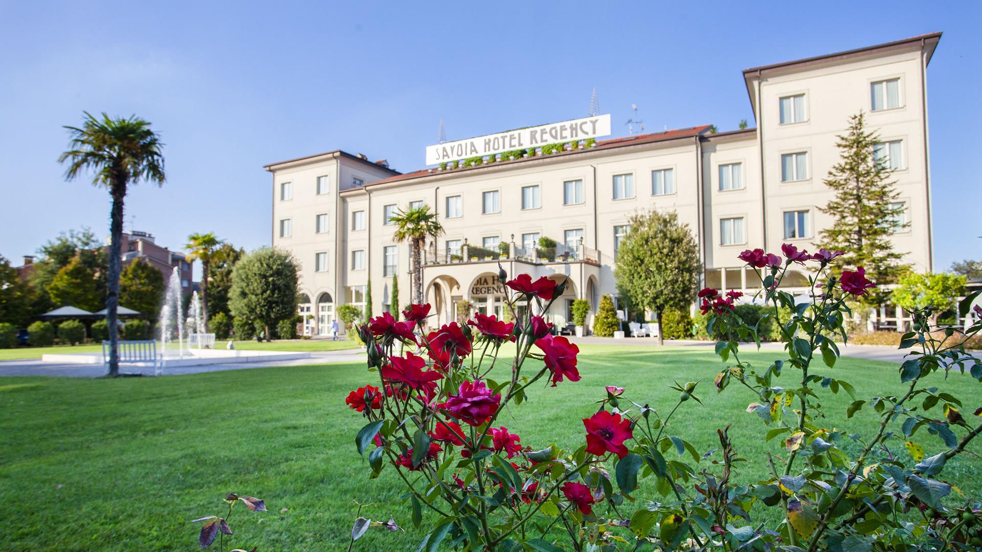 Hotel elegante con giardino curato e fontane, circondato da fiori e palme.