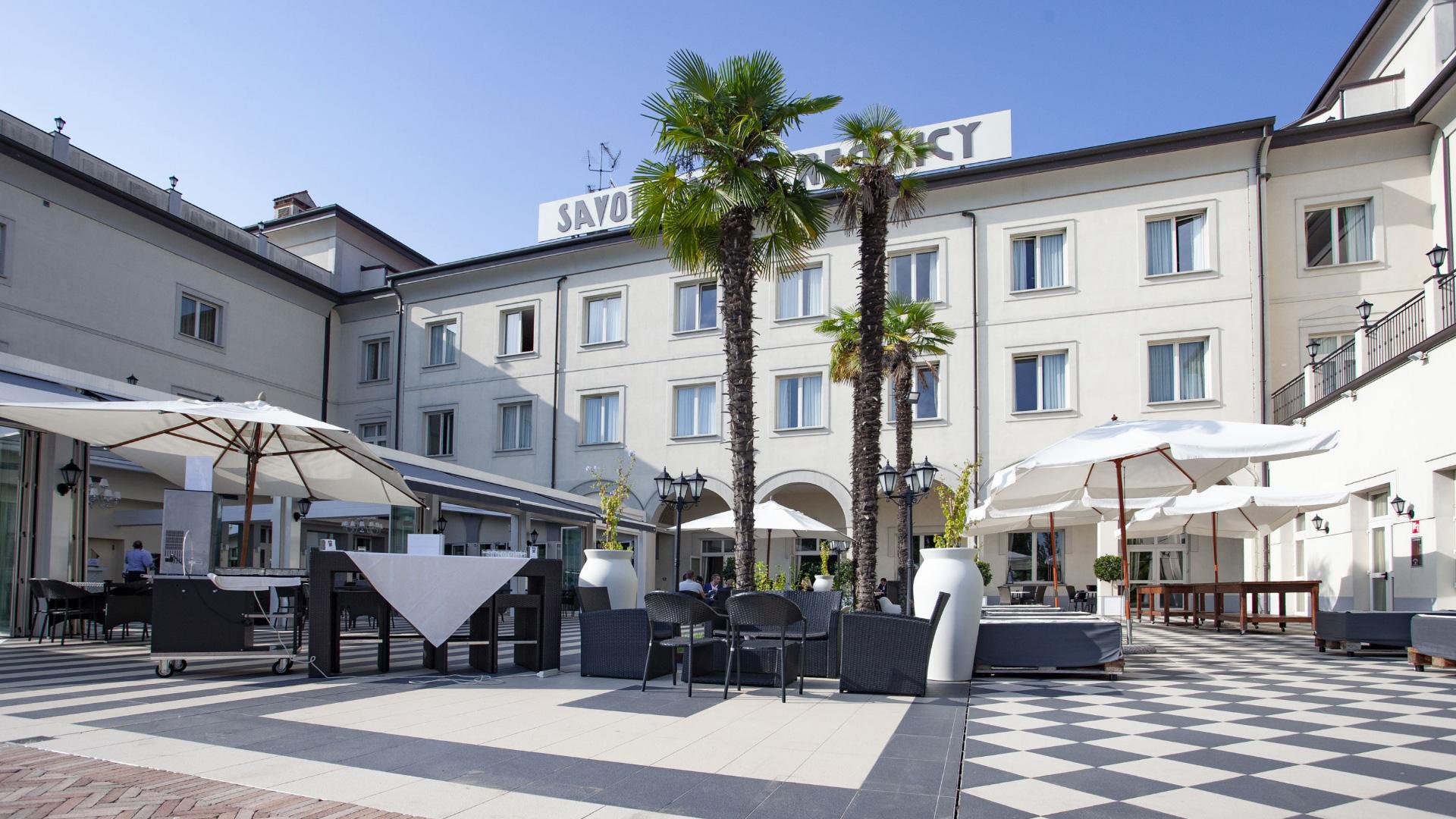 Cortile di un hotel con palme, sedie e ombrelloni bianchi.