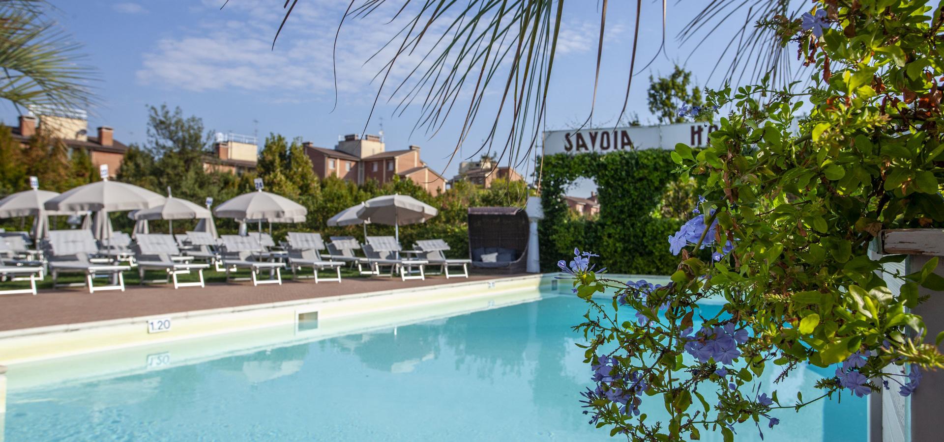 Outdoor pool with sunbeds and umbrellas, greenery, and clear sky.