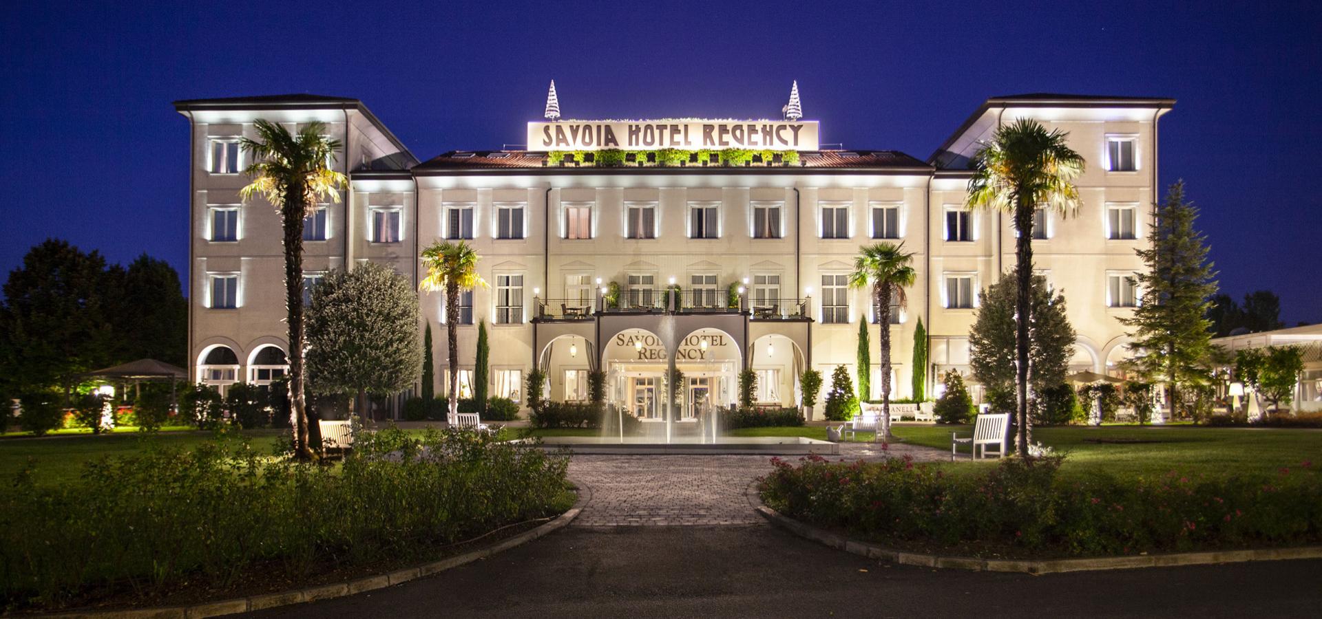Elegante hotel illuminato di notte con palme e giardino curato.