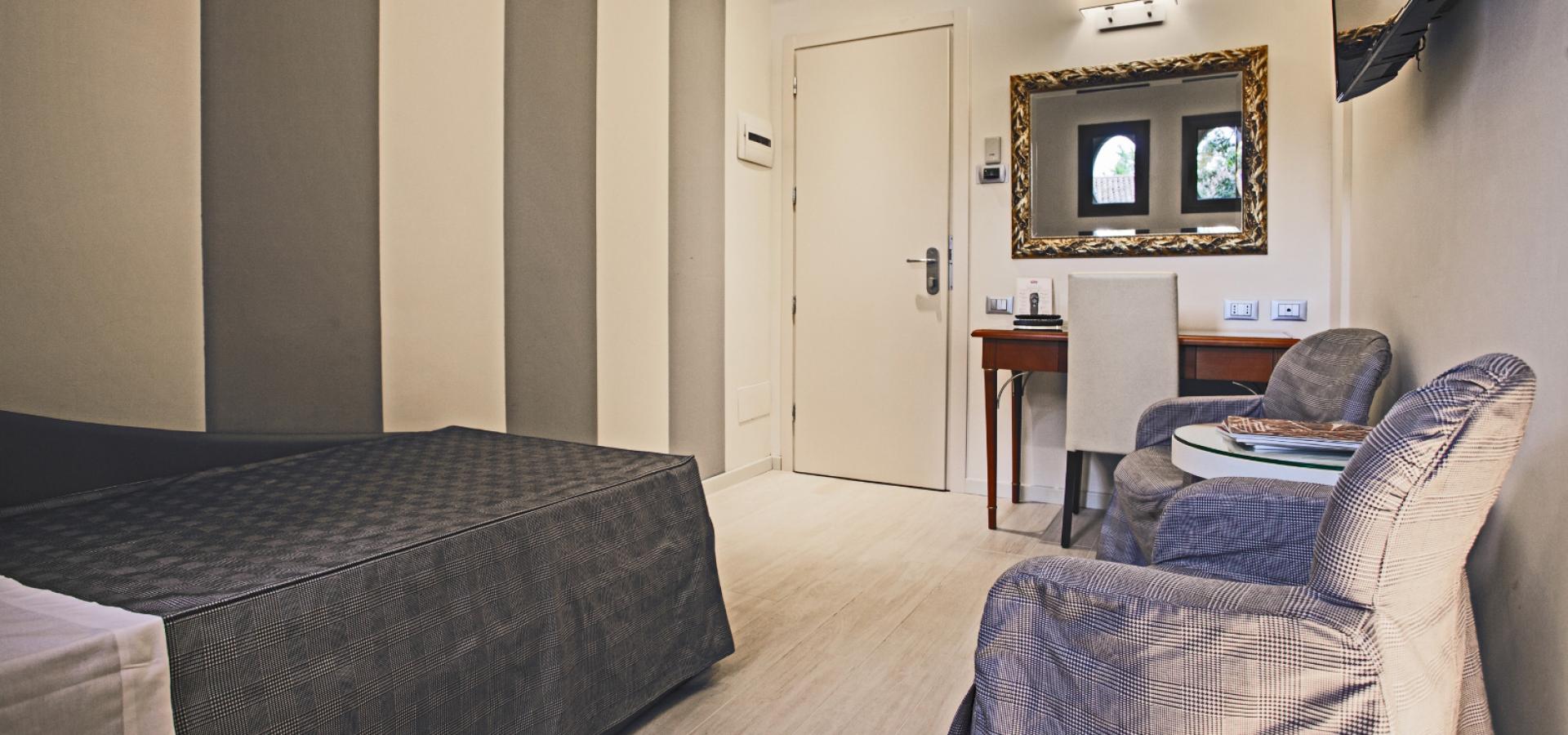 Modern hotel room with bed, desk, armchairs, and decorative mirror.