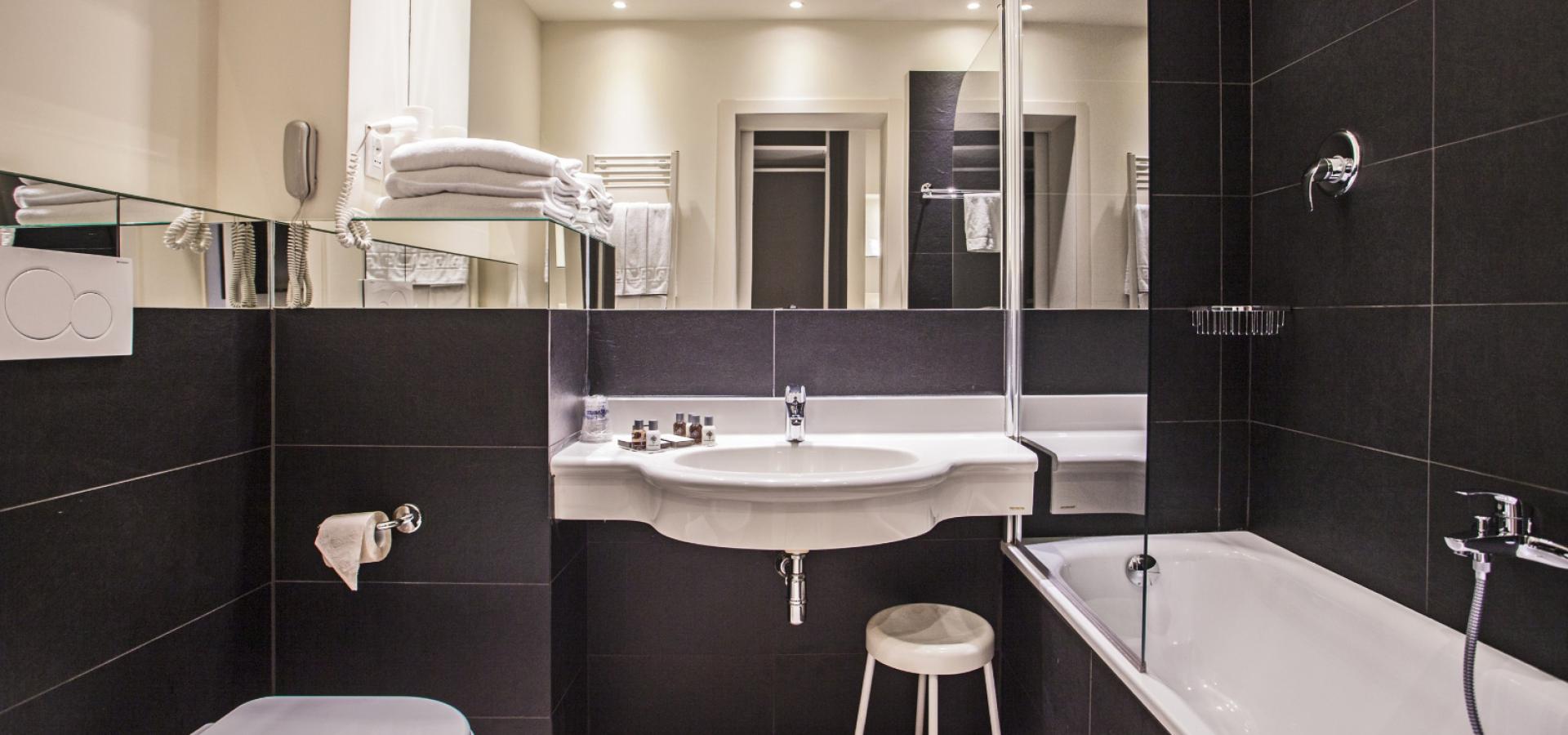 Modern bathroom with black tiles and white fixtures, large mirror, and shower tub.