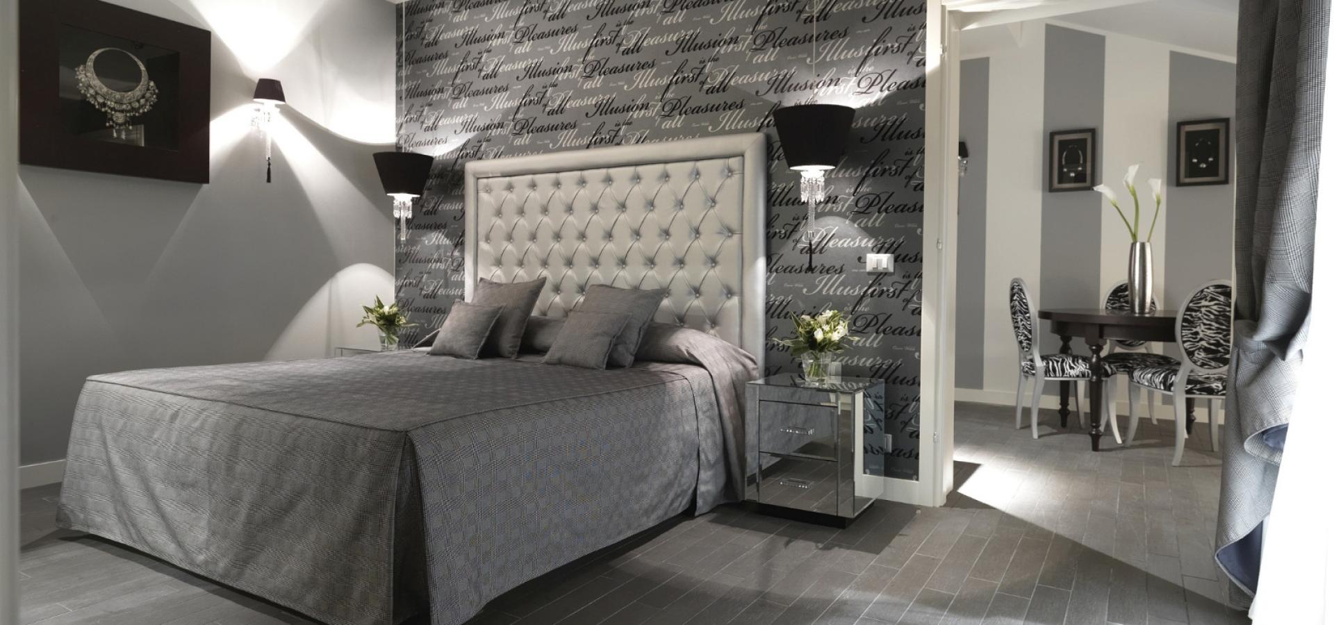 Modern bedroom with grey bed, scripted wallpaper, and adjacent dining area.