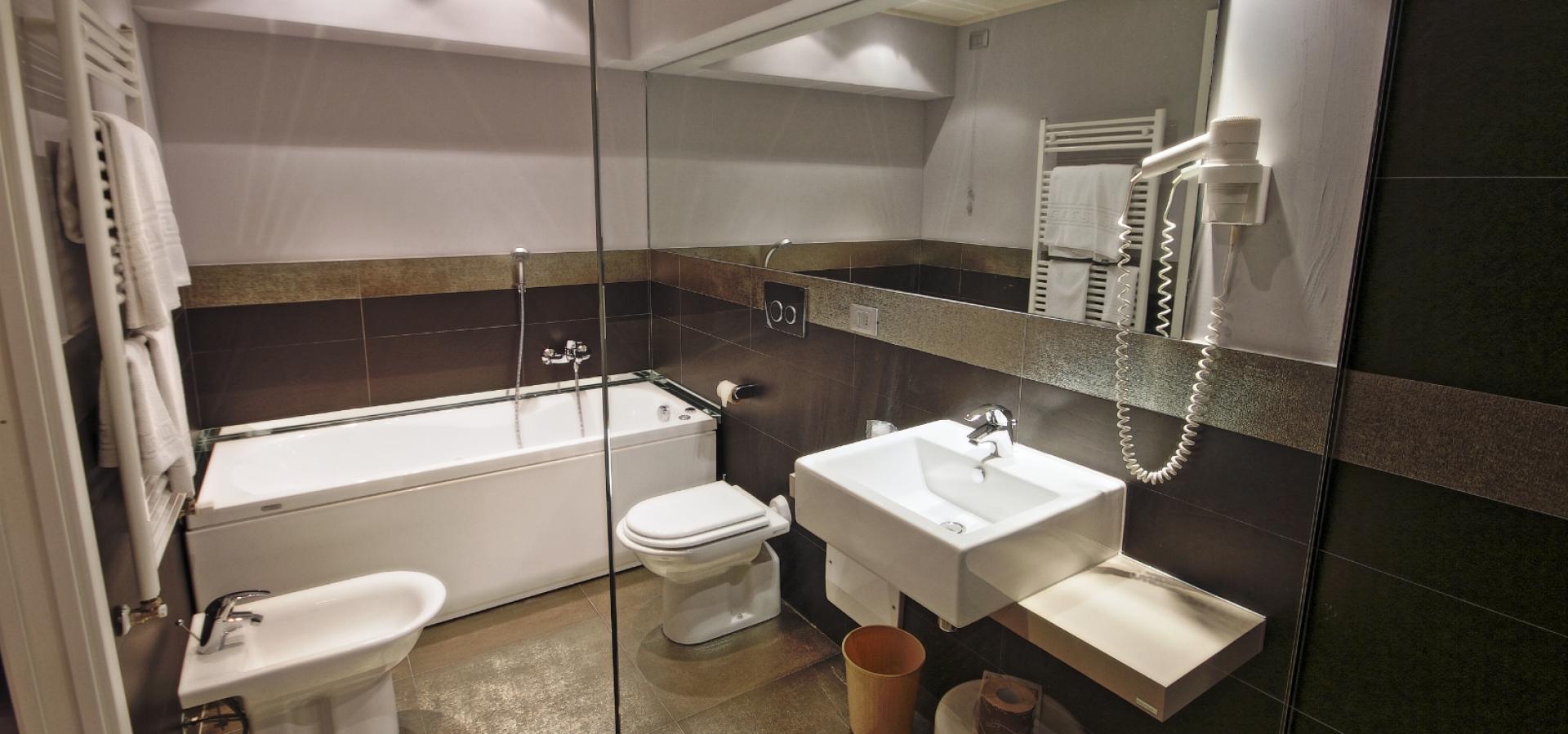 Modern bathroom with bathtub, sink, toilet, bidet, large mirror, and hairdryer.