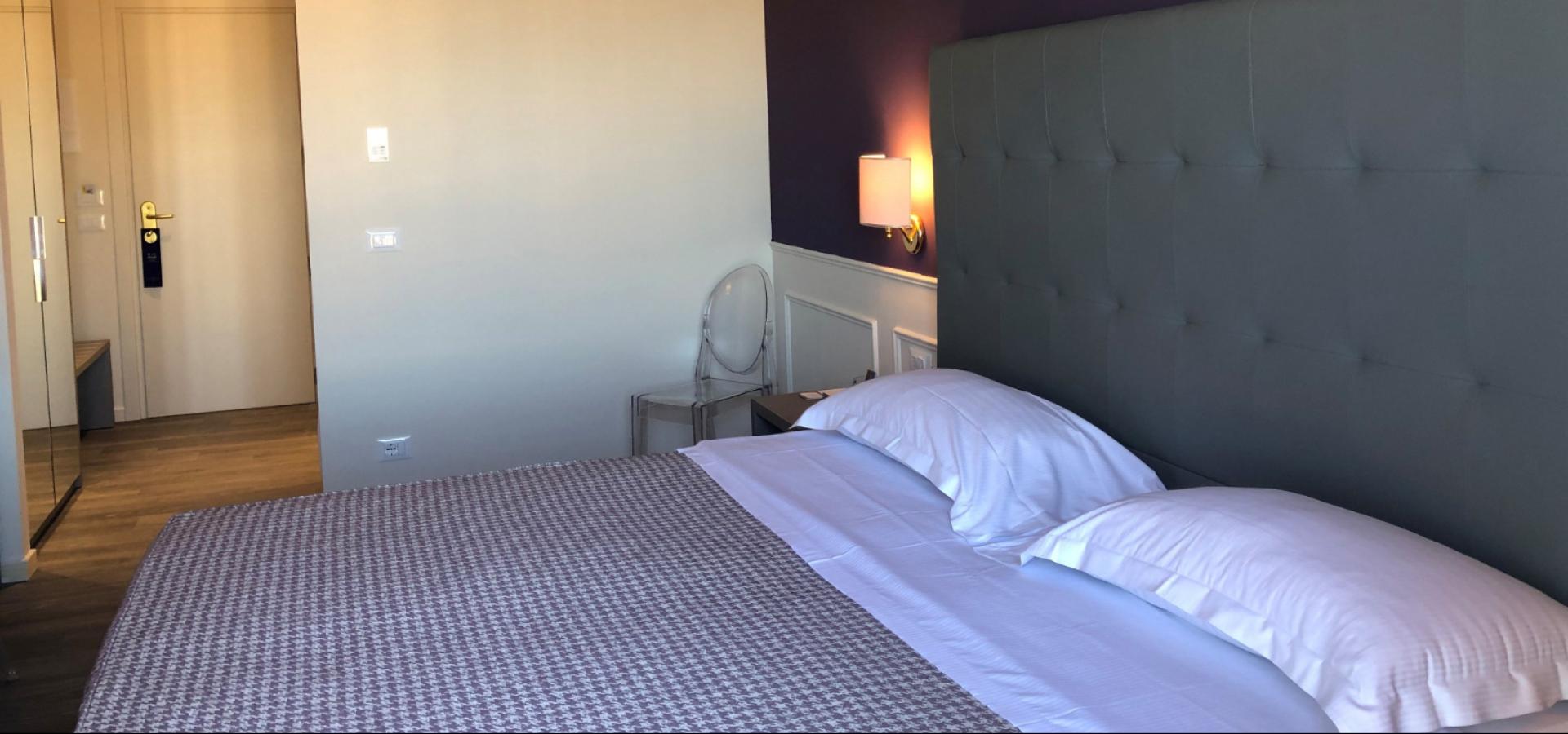 Modern hotel room with double bed, upholstered headboard, and purple wall.