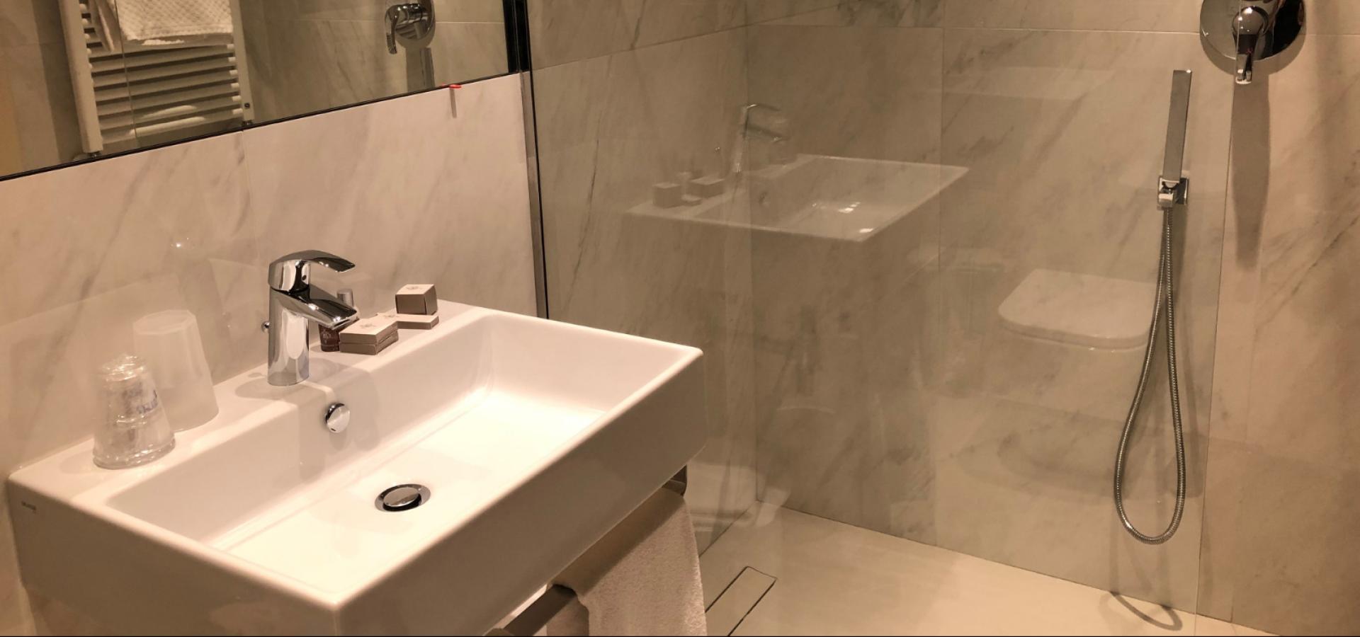 Modern bathroom with sink, rain shower, and marble walls.