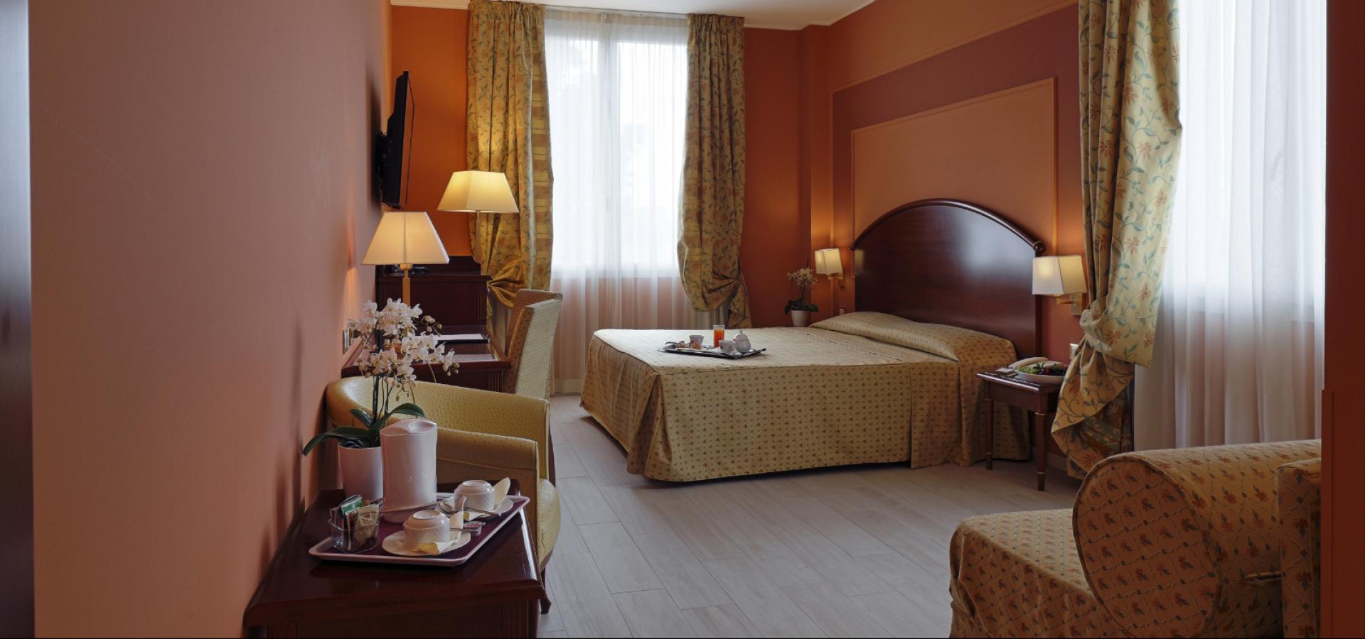 Hotel room with double bed, floral curtains, and elegant furniture.