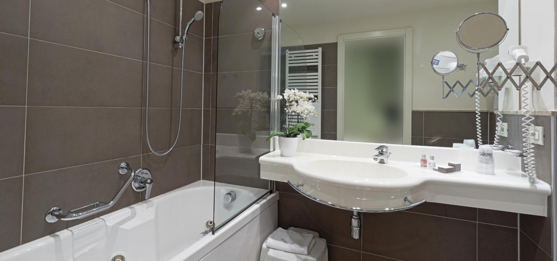 Modern bathroom with bathtub, shower, mirror, and sink with flowers and accessories.