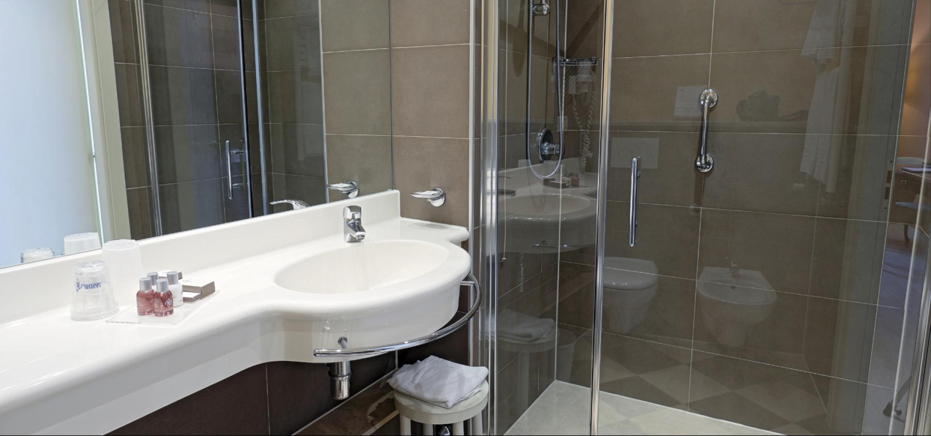 Bagno moderno con doccia in vetro, lavabo bianco e accessori da toilette.