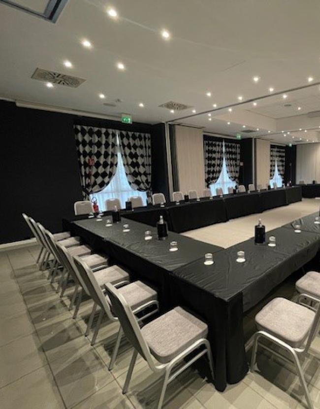 Conference room with U-shaped tables, grey chairs, and black and white decorations.