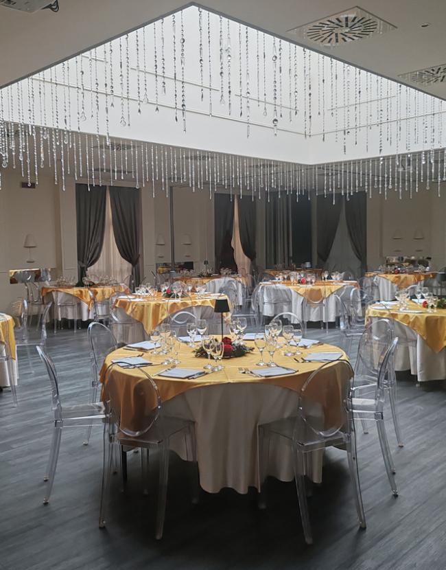 Elegante sala da pranzo con tavoli rotondi apparecchiati e decorazioni scintillanti sul soffitto.