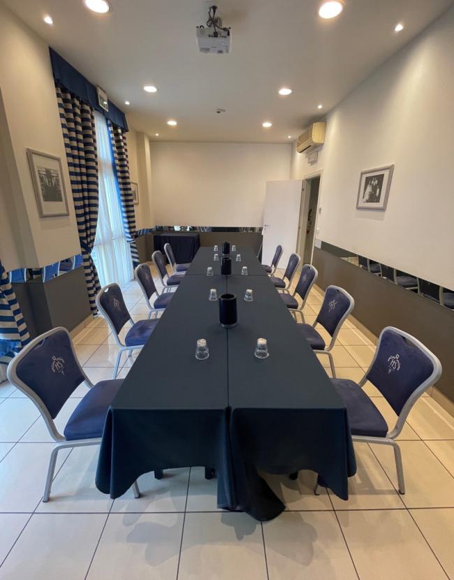 Sala riunioni con tavolo rettangolare, sedie blu e proiettore a soffitto.