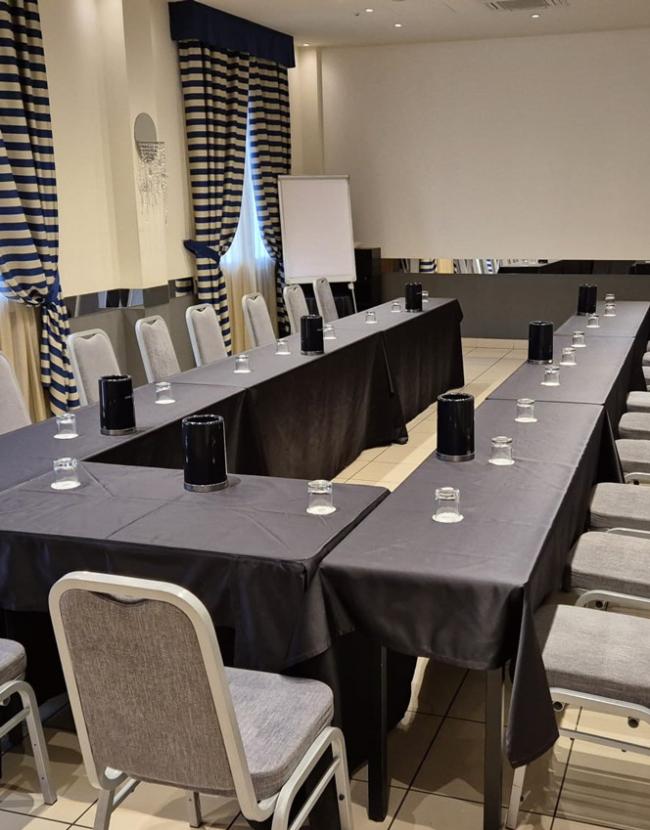Sala riunioni con tavoli disposti a U, sedie grigie e decorazioni eleganti.