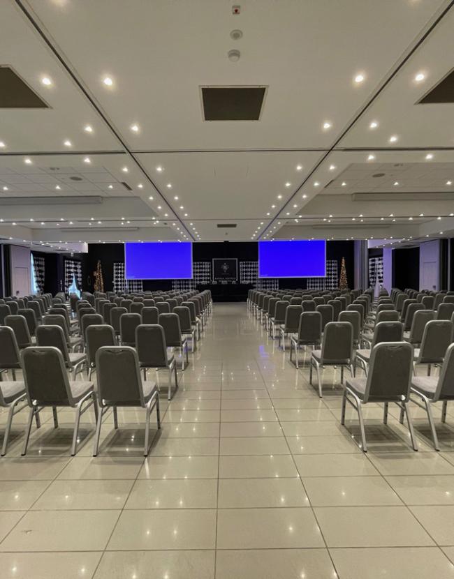 Sala conferenze con sedie disposte e schermo blu sullo sfondo.