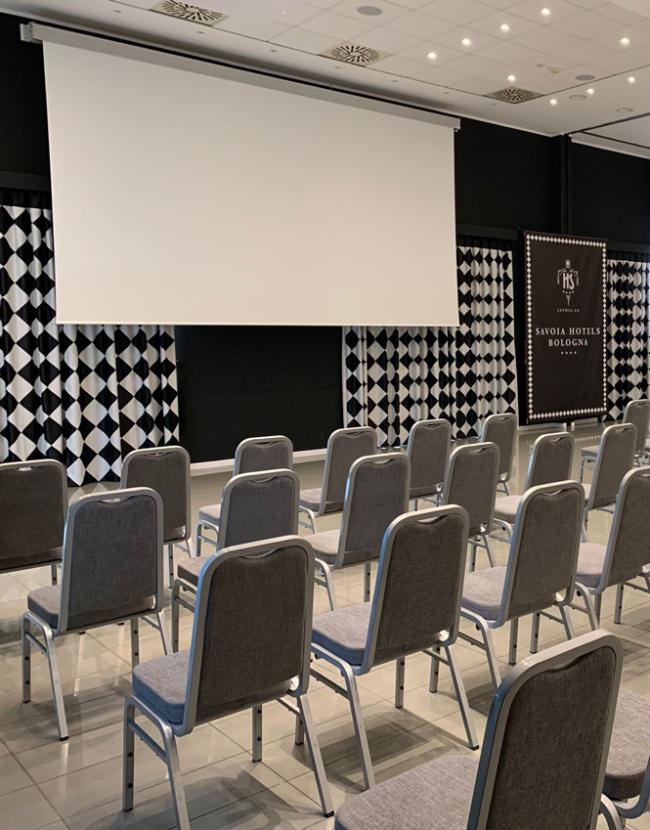Sala conferenze moderna con sedie grigie e schermi di proiezione.