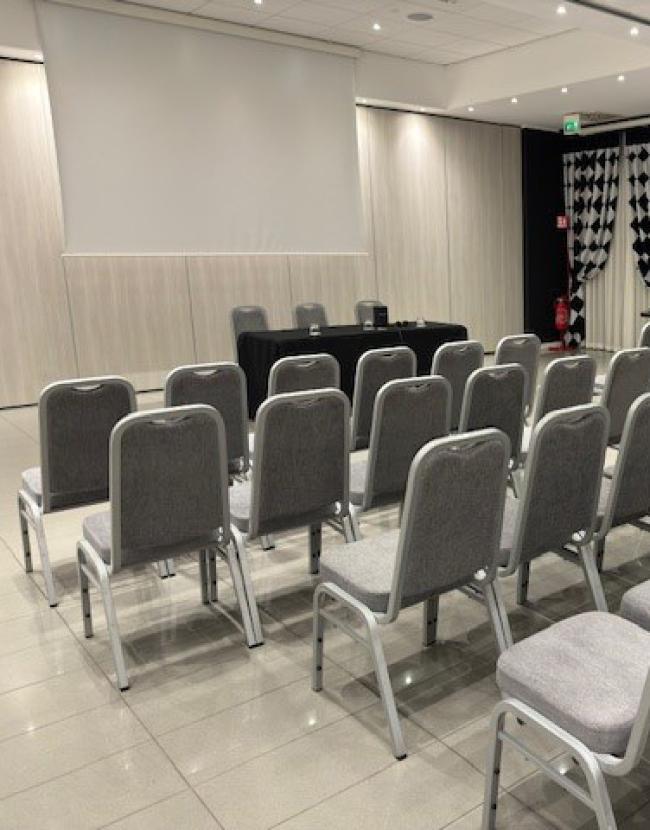 Sala conferenze con sedie grigie e schermo per presentazioni.