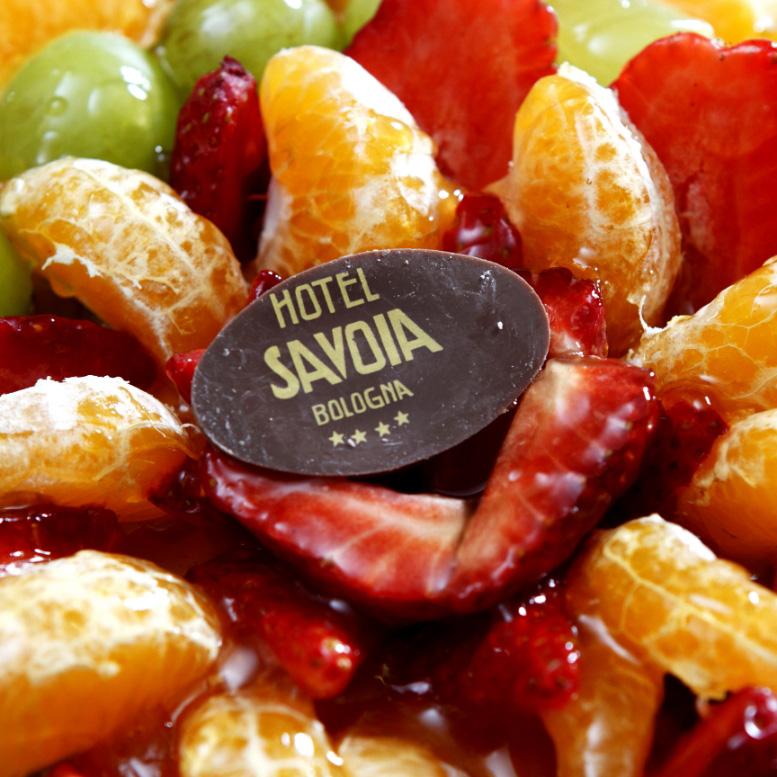 Fresh fruit decorated with Hotel Savoia Bologna label, strawberries, tangerines, and grapes.