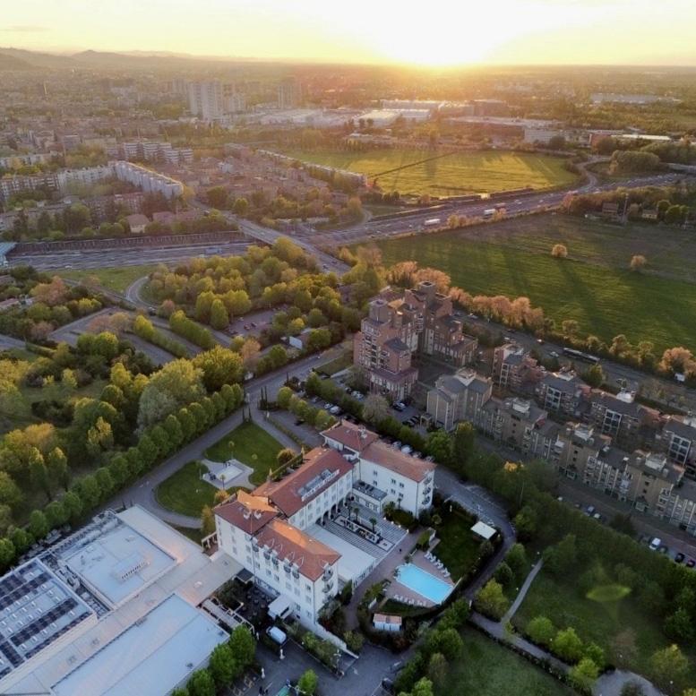 Aerial view of a city at sunset with buildings and green areas.