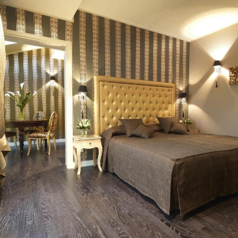 Elegant bedroom with striped walls, upholstered headboard, and wooden floor.